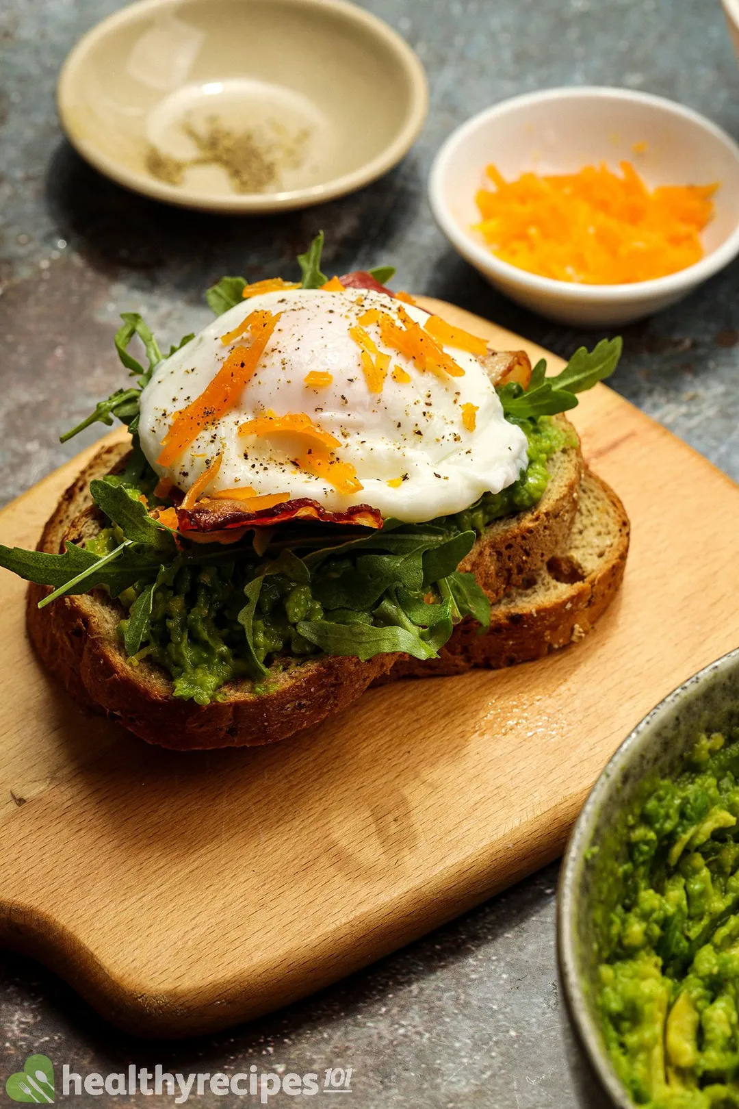 fried bacon and poached egg on top of two bread slices with mashed avocado on it