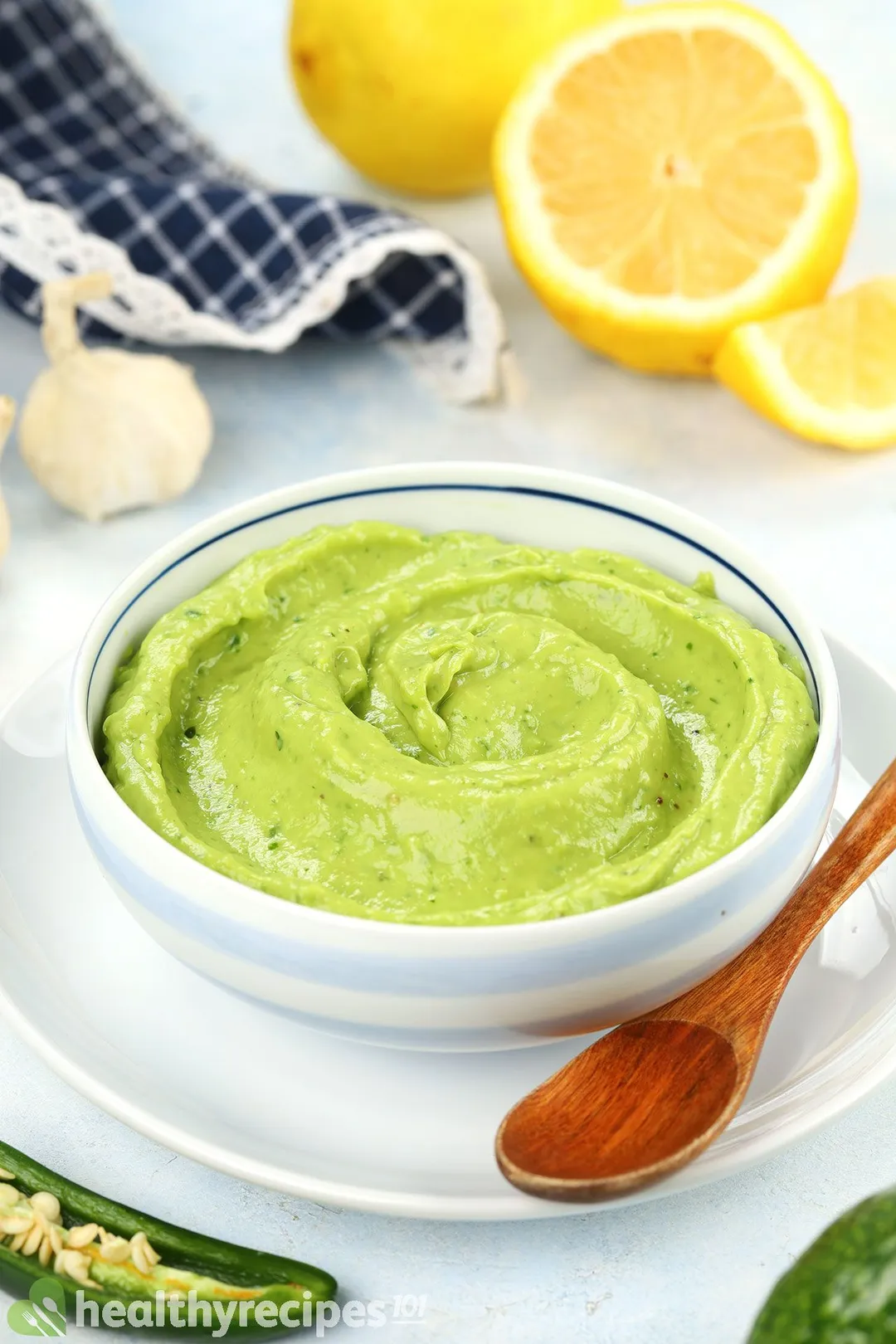 a bowl of avocado sauce on a plate decorated with a wooden spoon and half lemon slices