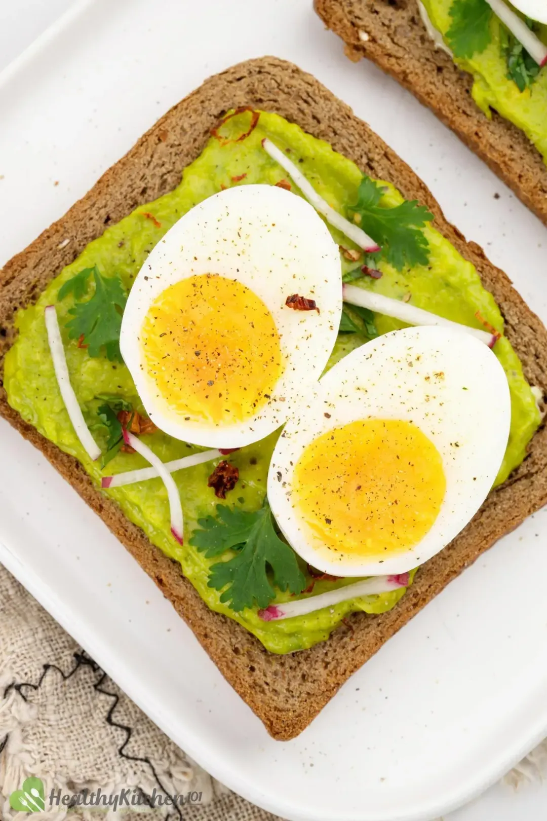 A top-down shot of two boiled egg slices on top of a slice of avocado toast, garnished with chili flakes and white radish
