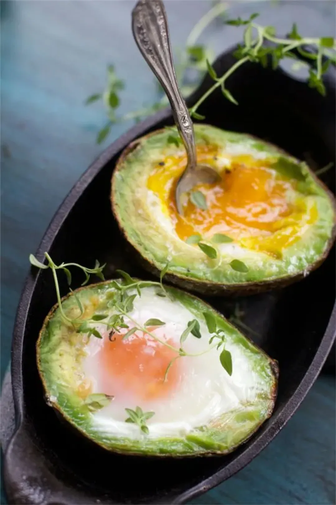 two half of avocado and egg on a tray, decorated with a spoon and fresh leaves