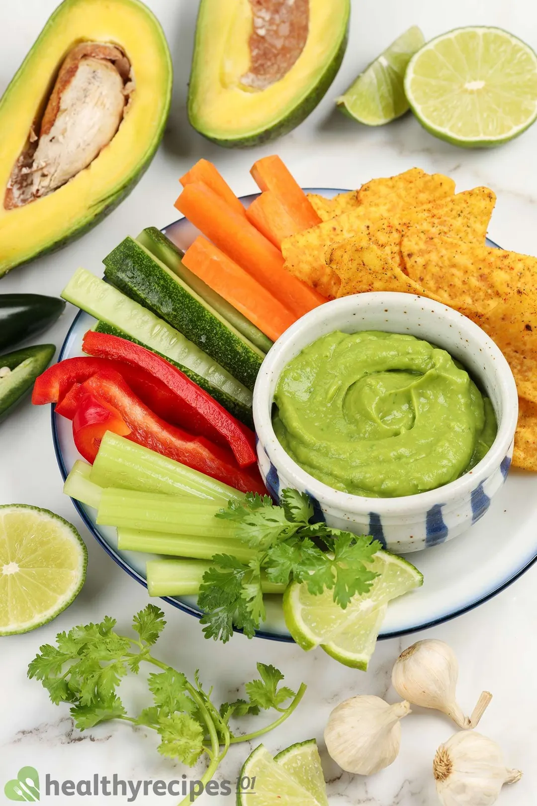 a bowl of avocado on a vegetables plate with two half avocado and half lemon, garlic, coriander for garnish