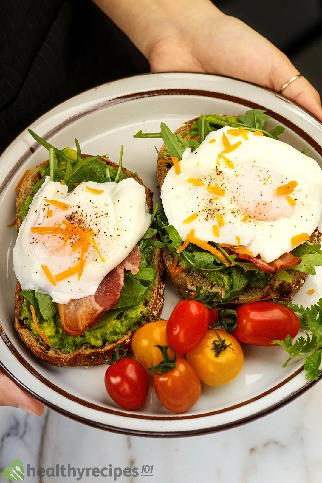 a hand holding a plate with two poached egg on bread decorated by cherry tomatoes