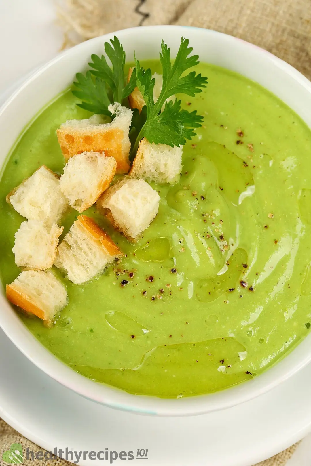 a bowl of avocado soup with croutons and coriander for garnish
