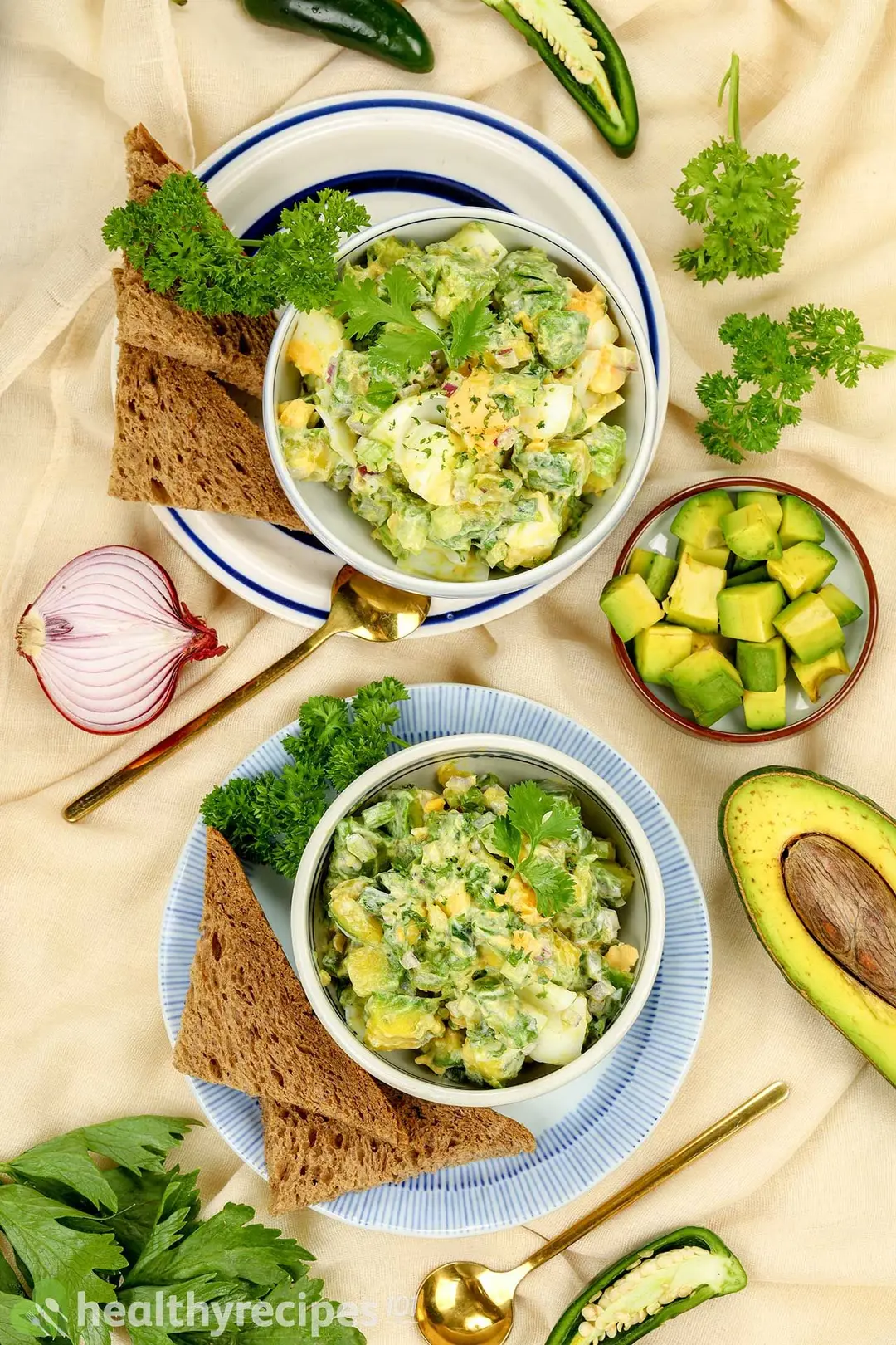 two plate with toast and a bowl of avocado salad on it, decorated by pepper, two spoon, a small avocado bowl and half avocado