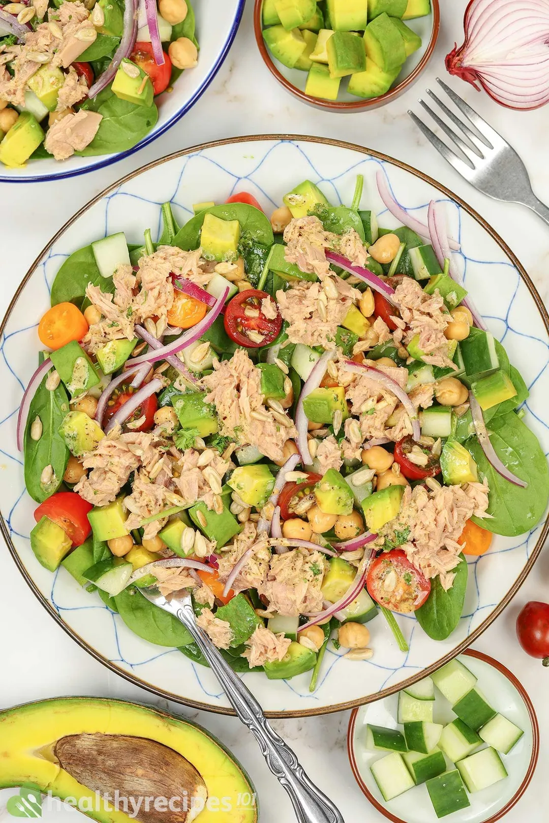 a plate of avocado cubes and canned tuna with half tomatoes, chick pea, spinach leaves and sun flower seeds