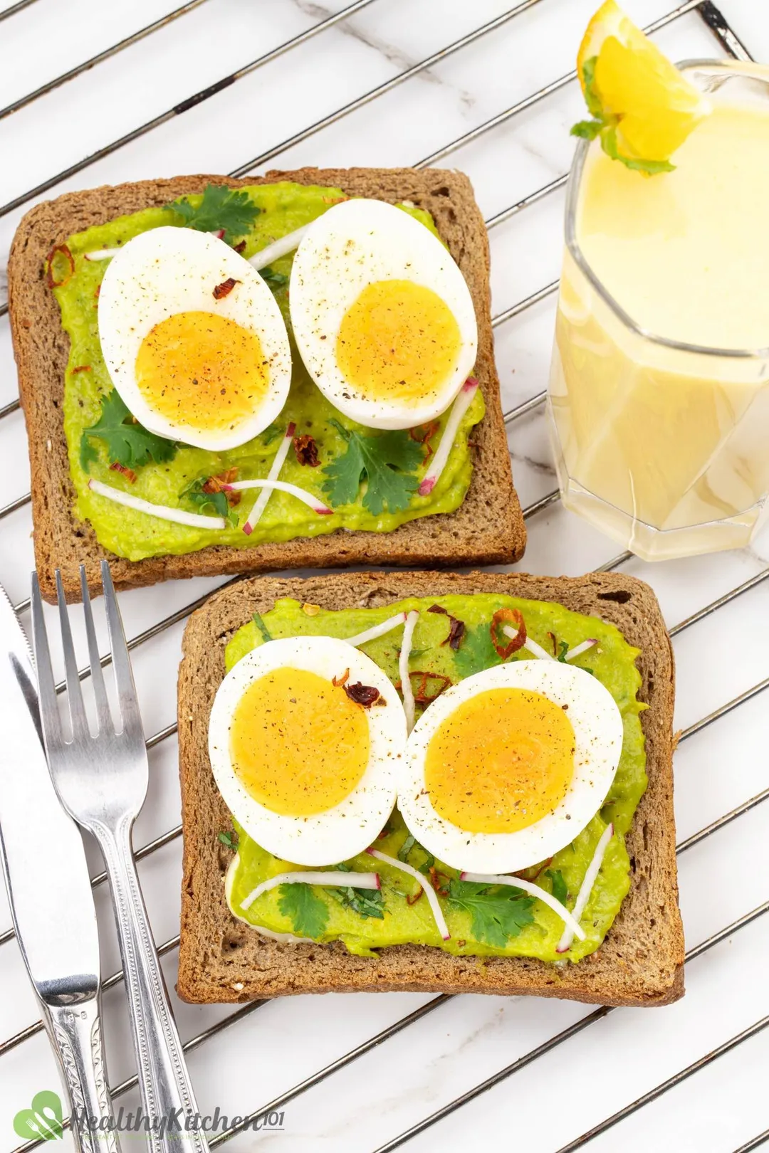 four half of boiled egg on two pieces of sandwich with mashed avocado on it a knife and fork, and a glass of milk for decorate