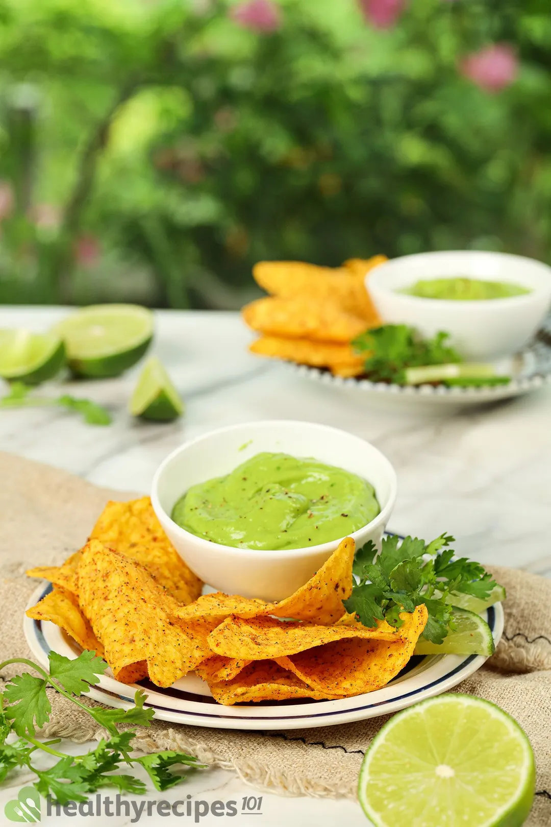 a bowl of avocado crema on a plate with tortilla chips, lemon slices in background