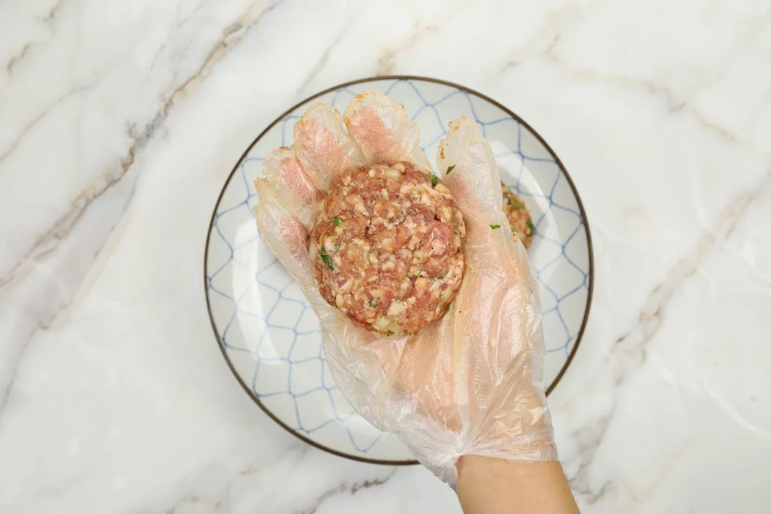 a hand with glove holding a patty on top of a plate
