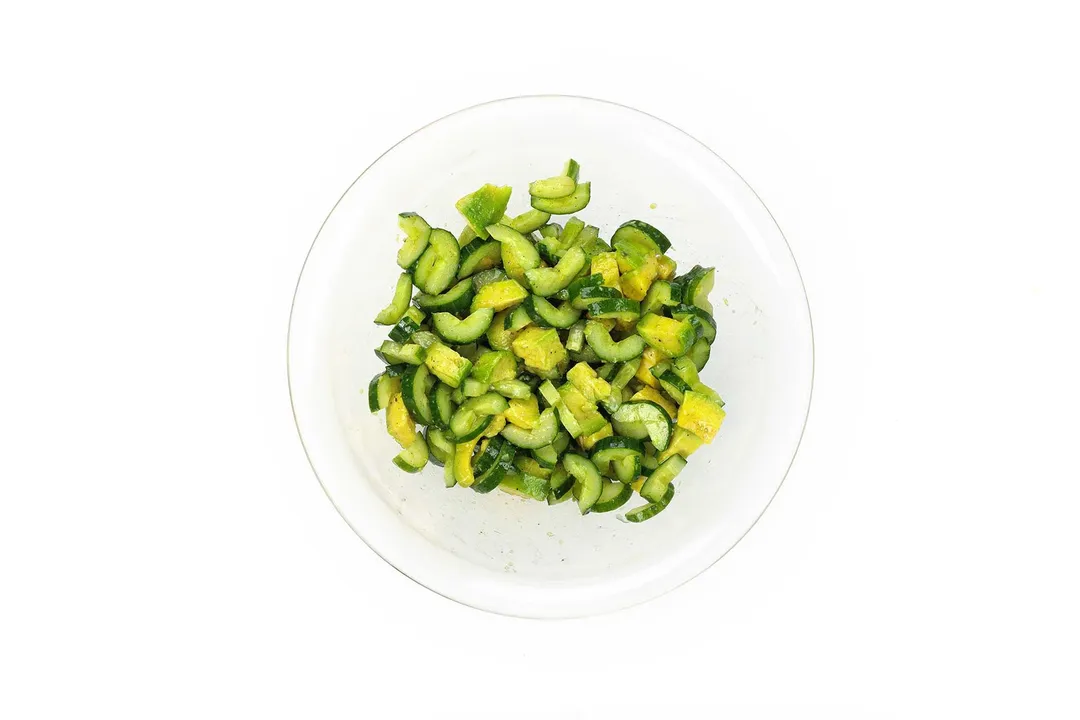 A large glass bowl filled with half-moon sliced cucumbers and avocado cubes