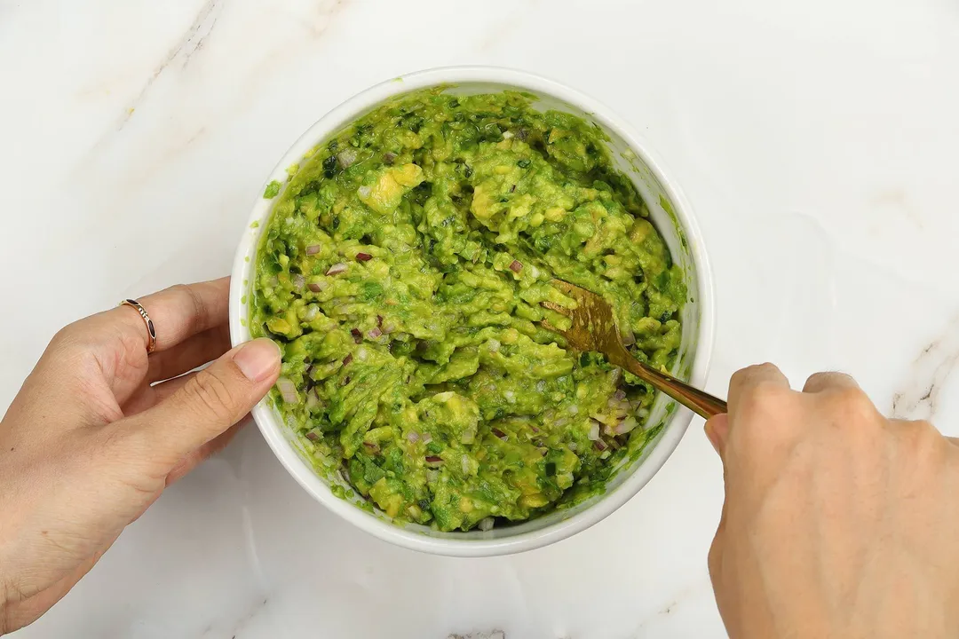 a hand holding a fork in a bowl of mash avocado