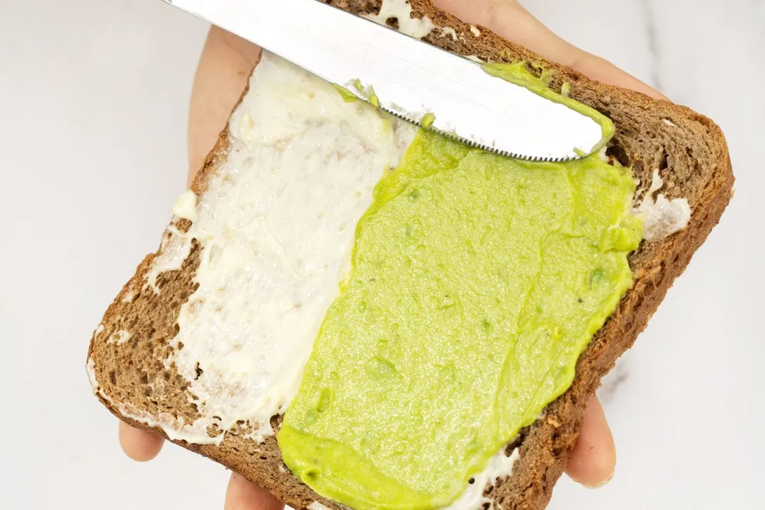 kitchen knife smearing mashed avocado and mayonnaise on toast