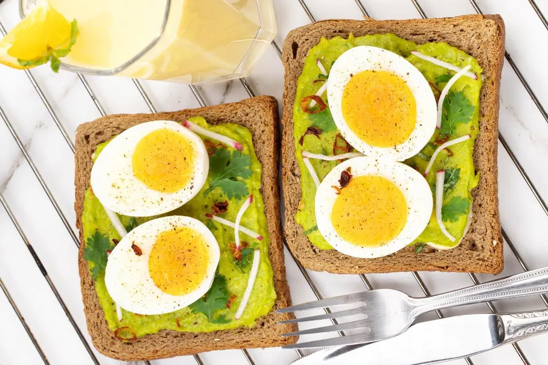 two toast with four half eggs and mashed avocado