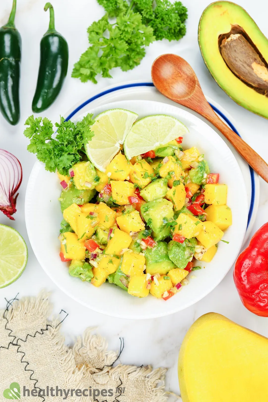 a plate of mango and avocado cubes decorated by lime slices, a wooden spoon, half avocado and pepper