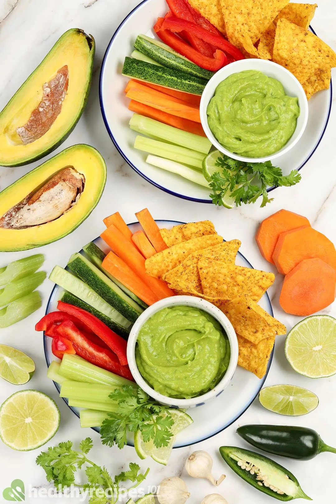 two plates avocado dip with vegetables and two half of avocado, lemon, pepper, cilantro for garnish