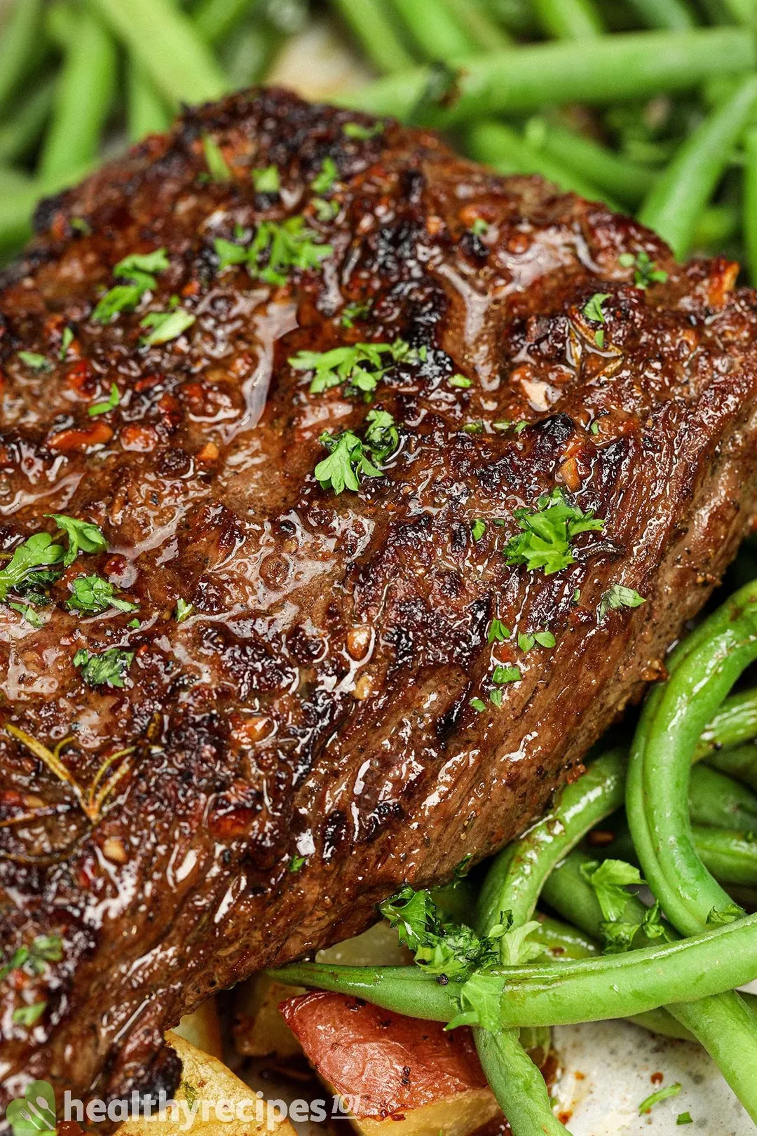 a cooked beef flank steak bedding on green bean and cubed potatoes