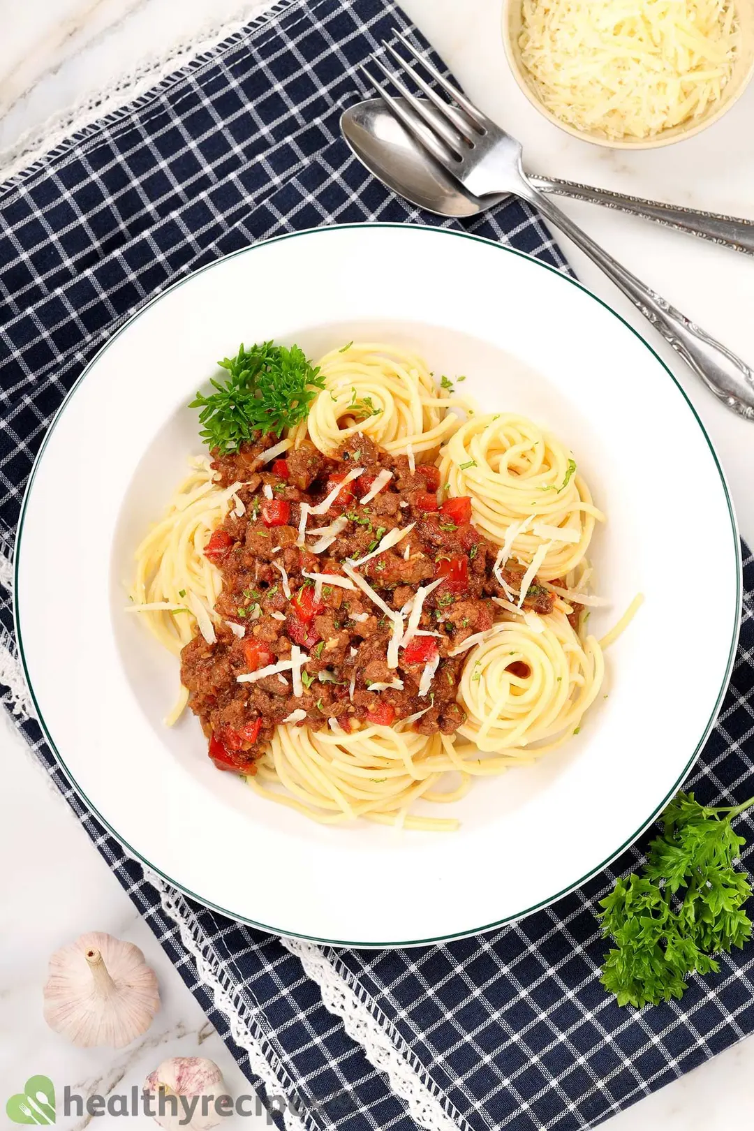 a plate of cooked pasta with ground beef, decorated with a spoon and fork, parsley and shredded parmesan cheese