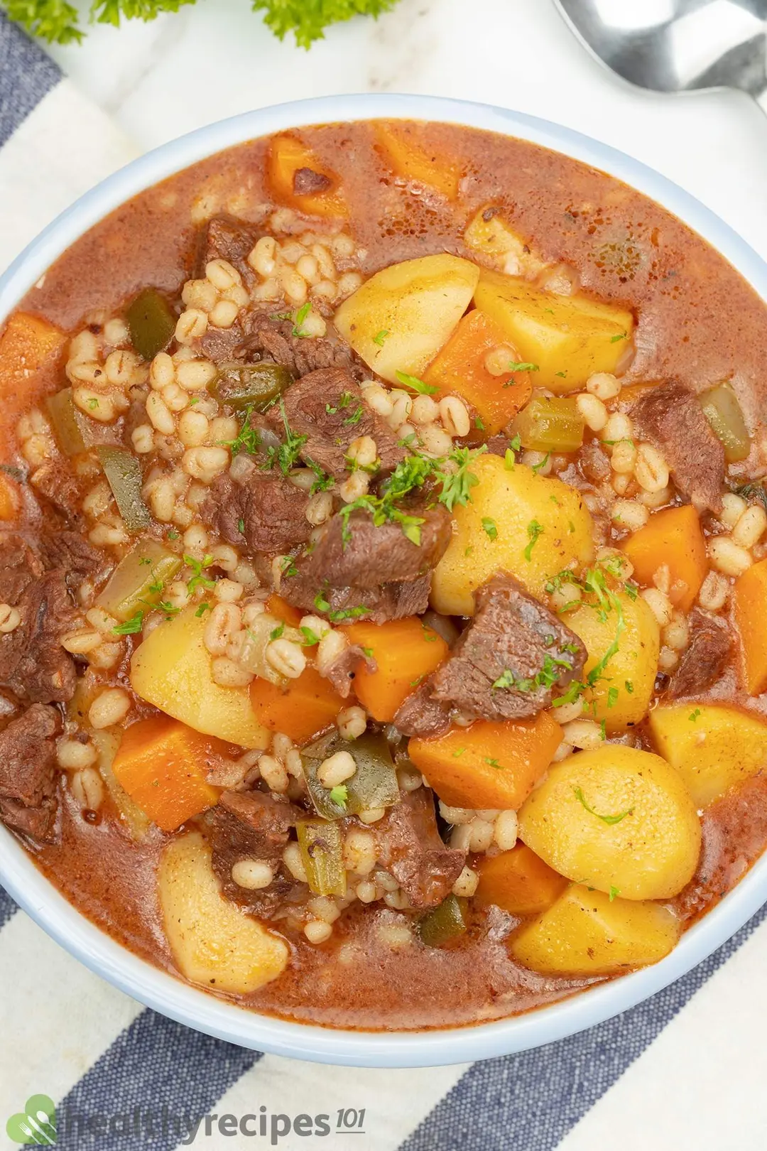 a bowl of cooked beef soup with cubed potatoes and carrot, barley