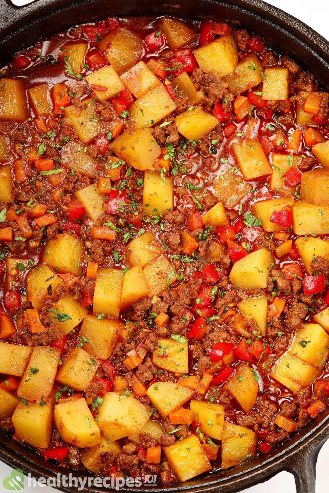 close-up shot of cooked cubed potatoes and ground beef with carrot and pepper in a cast iron skillet