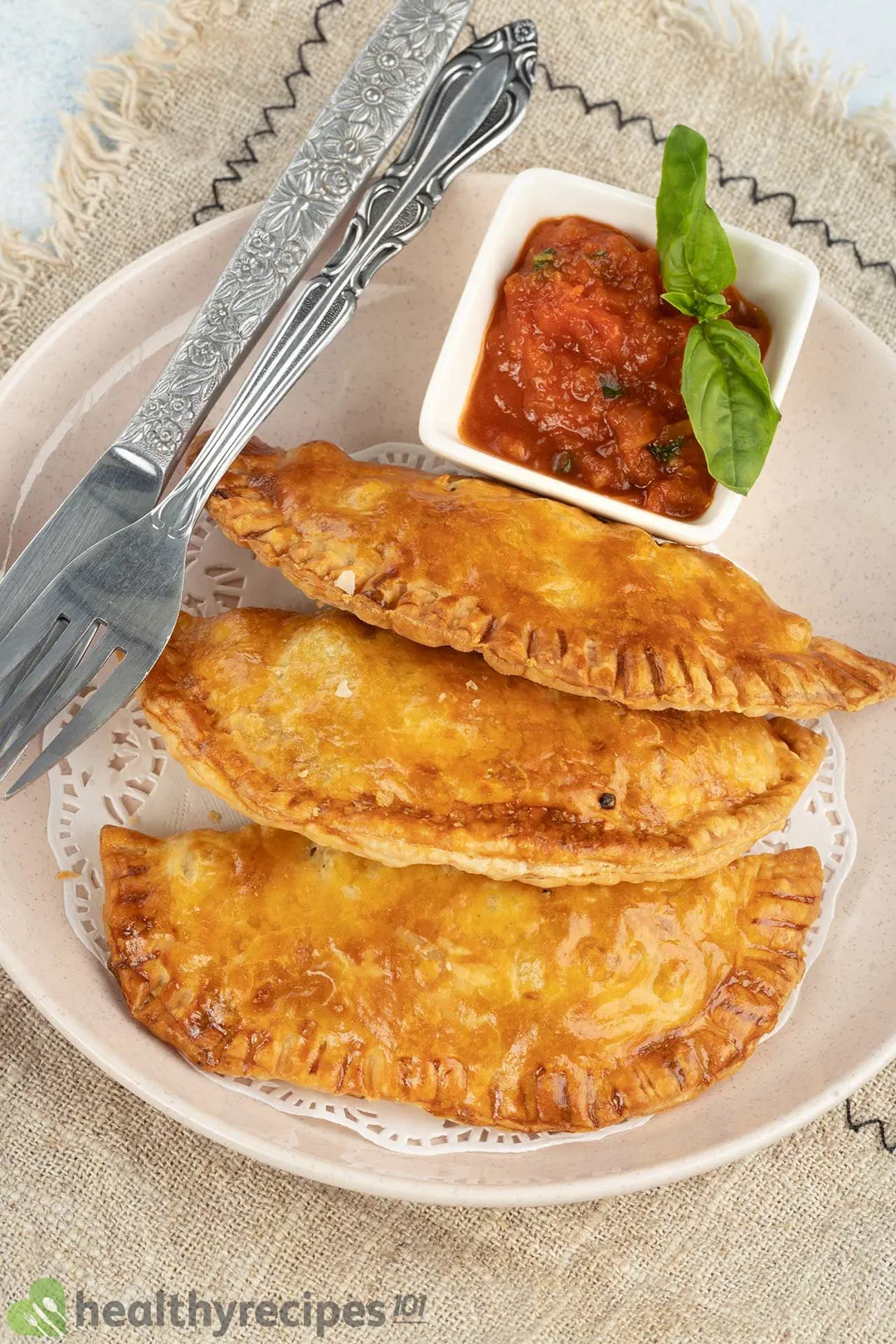 three empanadas on a plate next to small bowl of red sauce