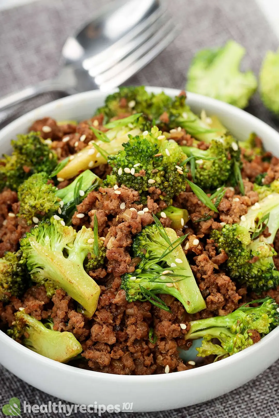 close-up view of a bowl of cooked ground beef and broccoli garnished by chopped scallion, sesame