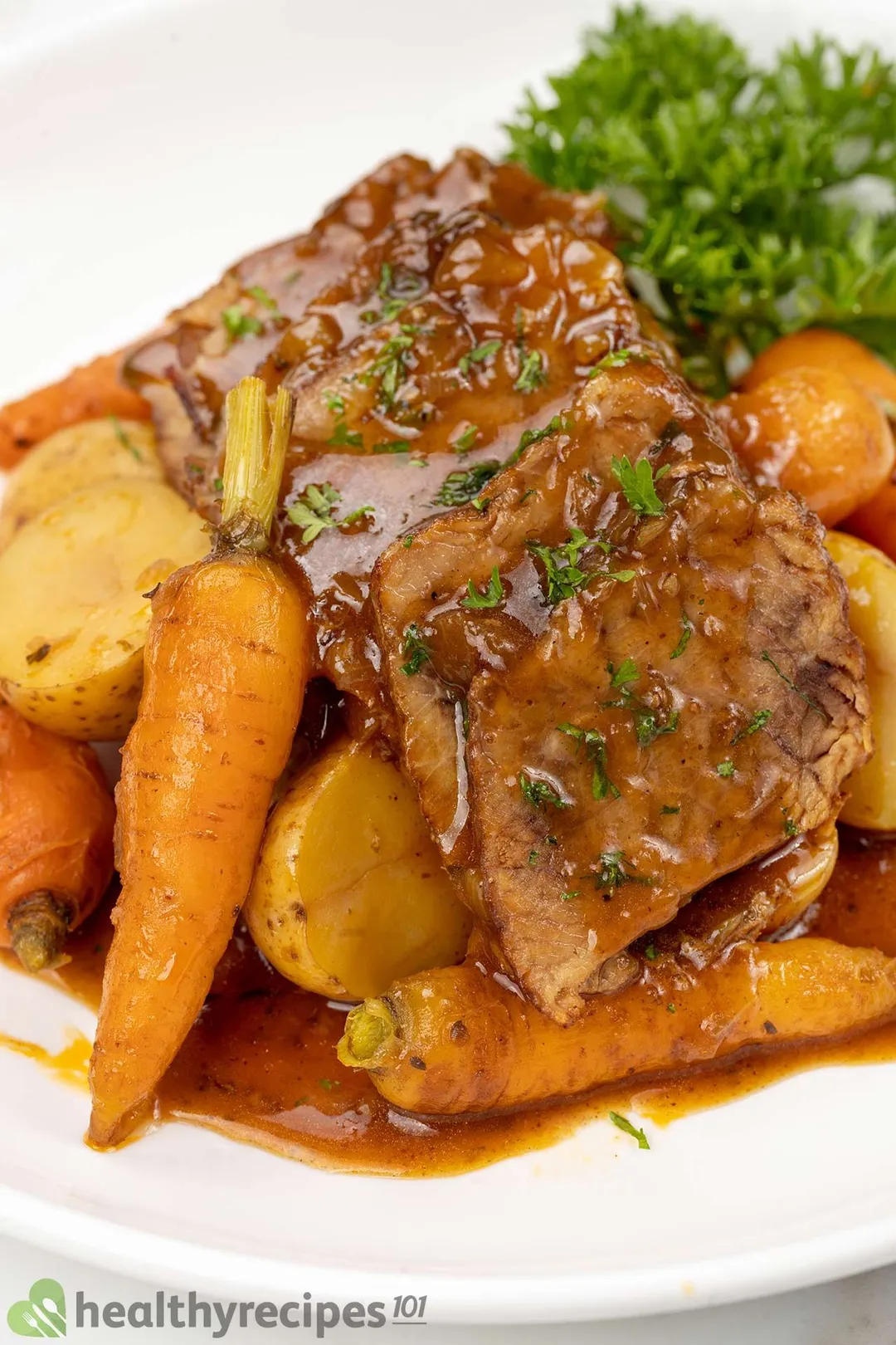 close-up shot of a plate of cooked beef brisket sliced and half potatoes, carrot and parsley for garnish