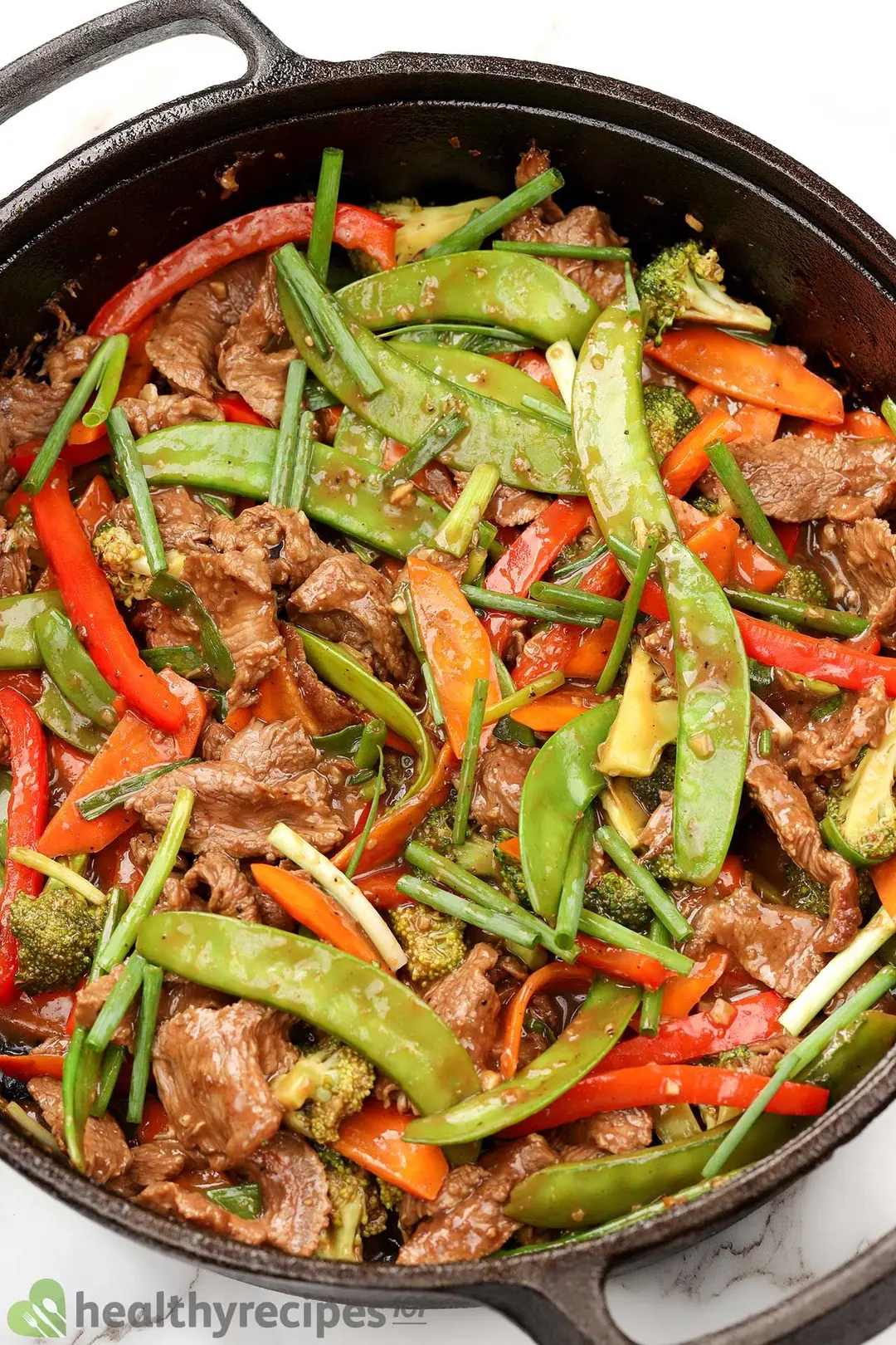 a cast iron skillet of cooked sliced beef, green bean sliced carrot and pepper, chopped scallion