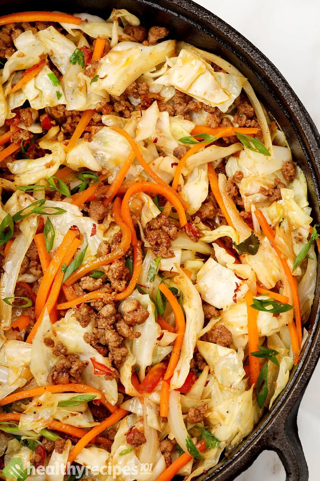 a cast iron of cooked cabbage and ground beef with julienned carrot and chopped scallion