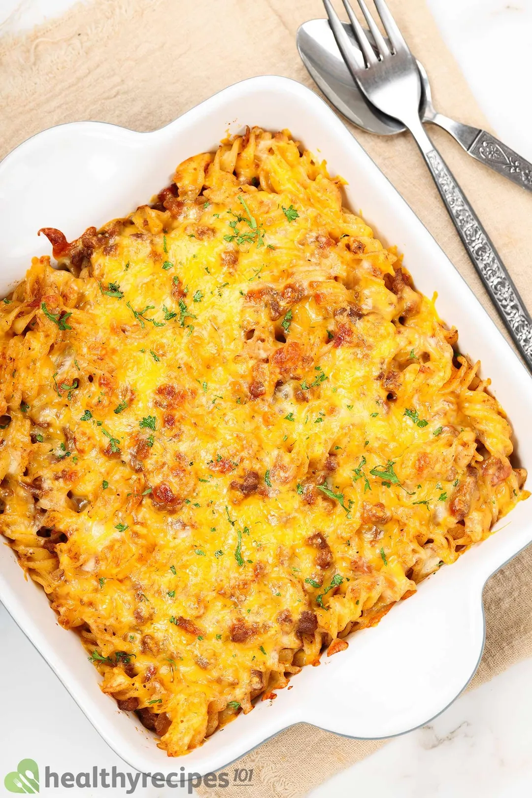cooked pasta with ground beef and cheese in a casserole decorated by a fork and spoon