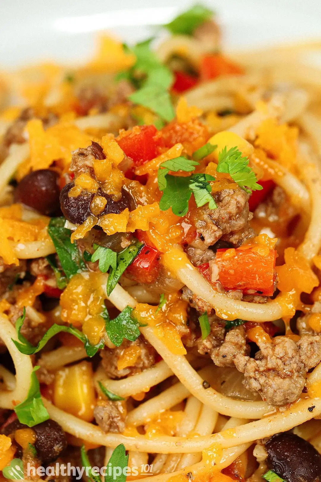 close-up view of cooked ground beef and pasta with cheddar cheese on top and chopped cilantro for garnish