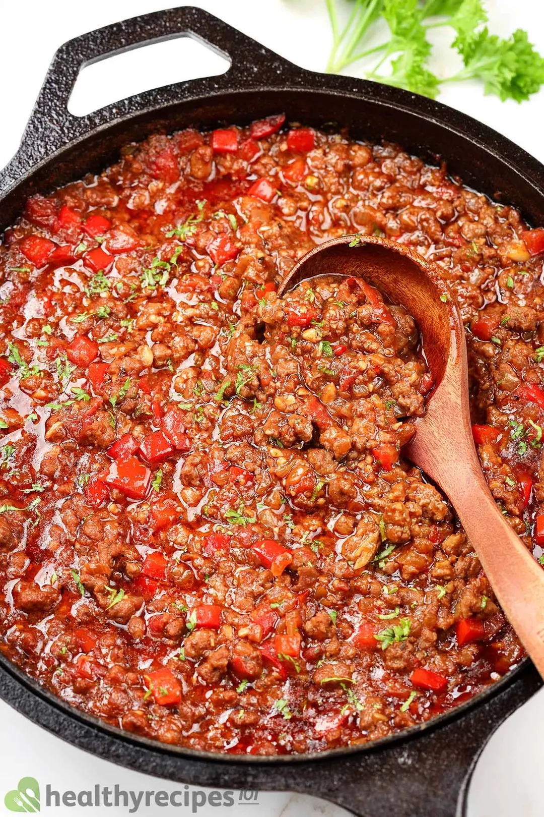 a cast iron skillet of cooked ground beef with pepper and a wooden spoon in it
