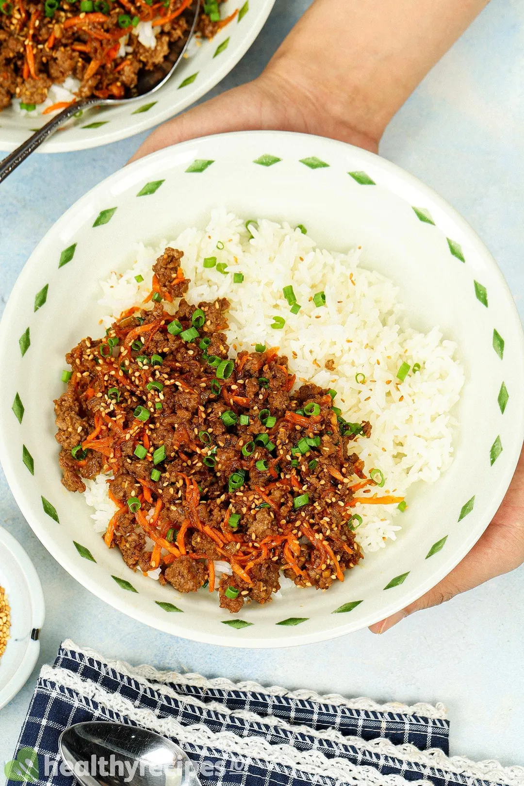 two hands holding a bowl of cooked ground beef and rice