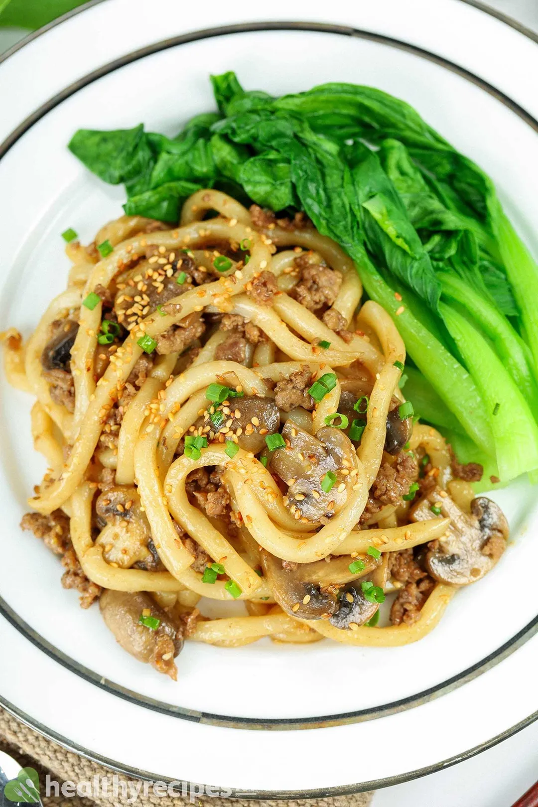 a plate with cooked beef, noodle and vegetable decorated with sesame seeds