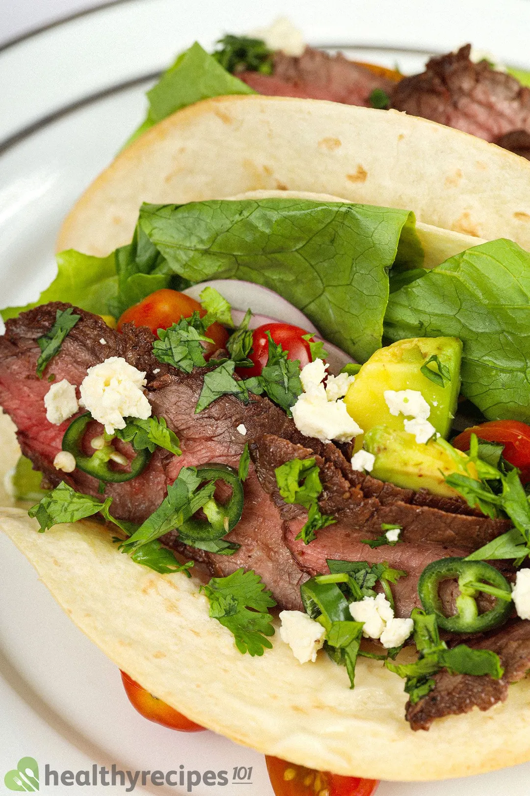 a plate have taco, lettuce, shaved beef, cherry tomatoes, cubed avocado, pepper slices and cheese 