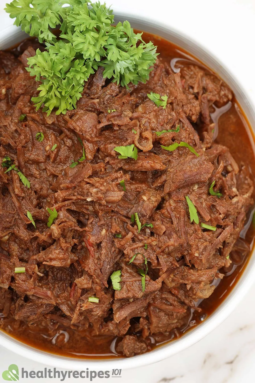 top view of a bowl of cooked shredded beef garnished by parsley