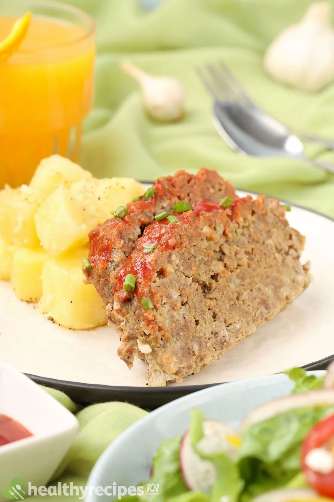 close-up shot of a plate with two pie of meatloaf and potatoes cubes on it, half orange juice glass in background