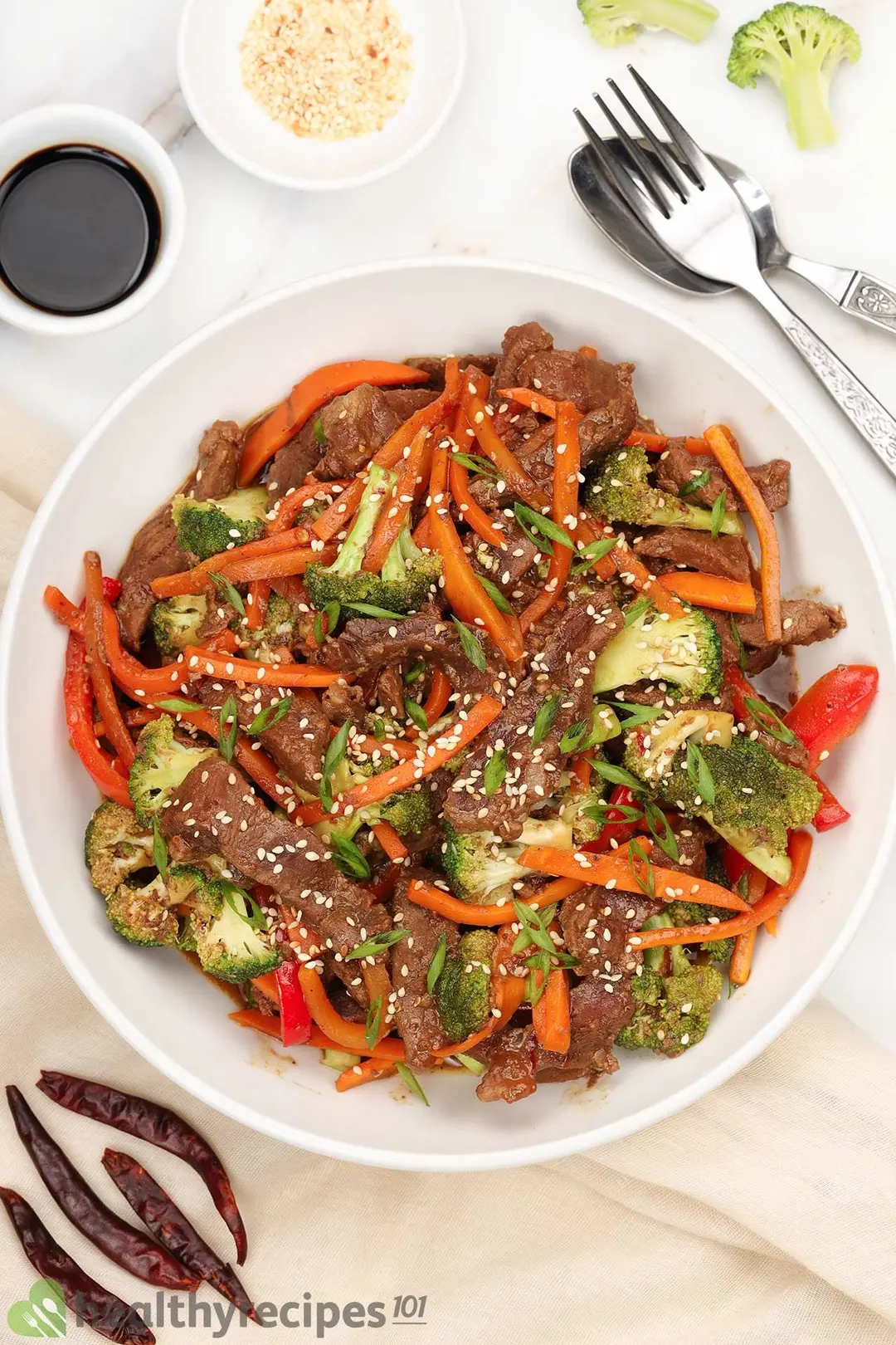 a plate of cooked beef with julienned carrot and bell pepper, chopped scallion and sesame seed