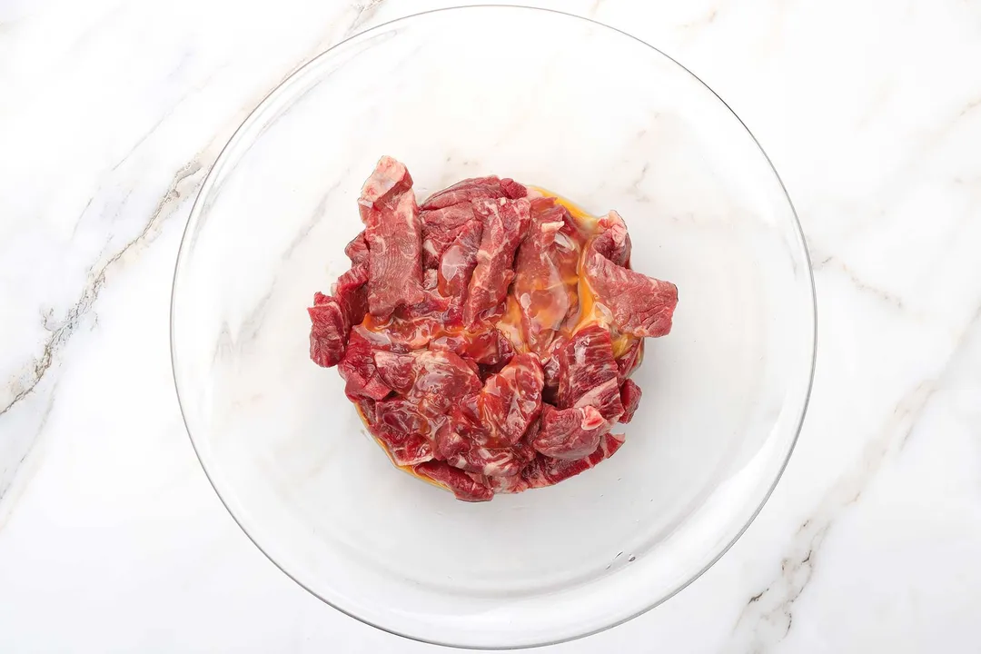 sliced beef chunk and beaten egg in a glass bowl