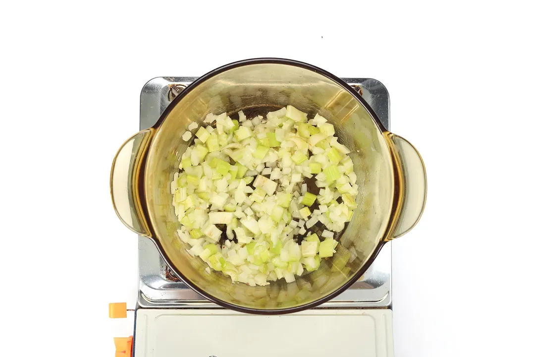 A glass saucepan filled with diced celery and diced onion cooking on a portable gas stove