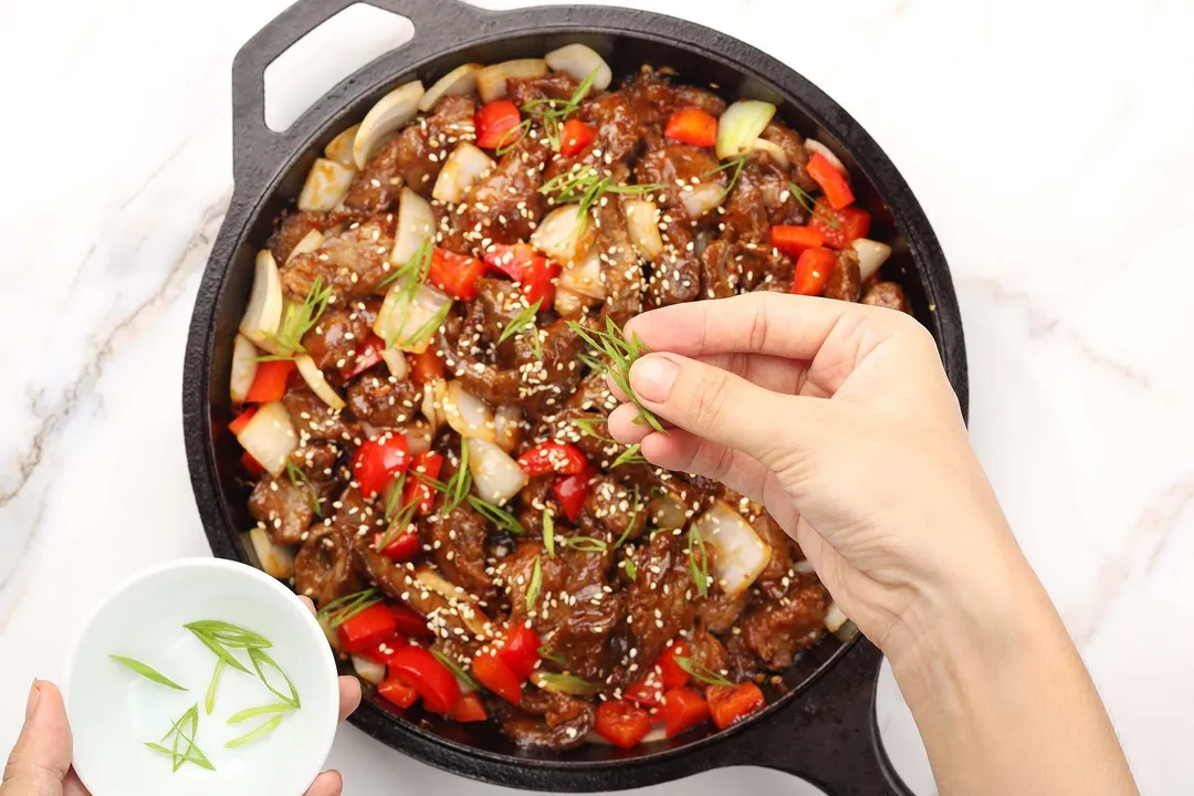 sprinkle chopped onion onto a cast iron skillet of beef and veggie