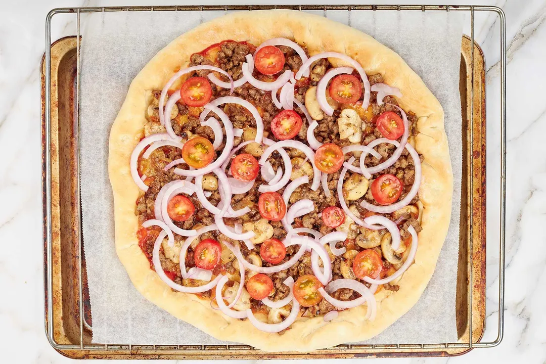 topping, cherry tomatoes and sliced red onion on top of pizza
