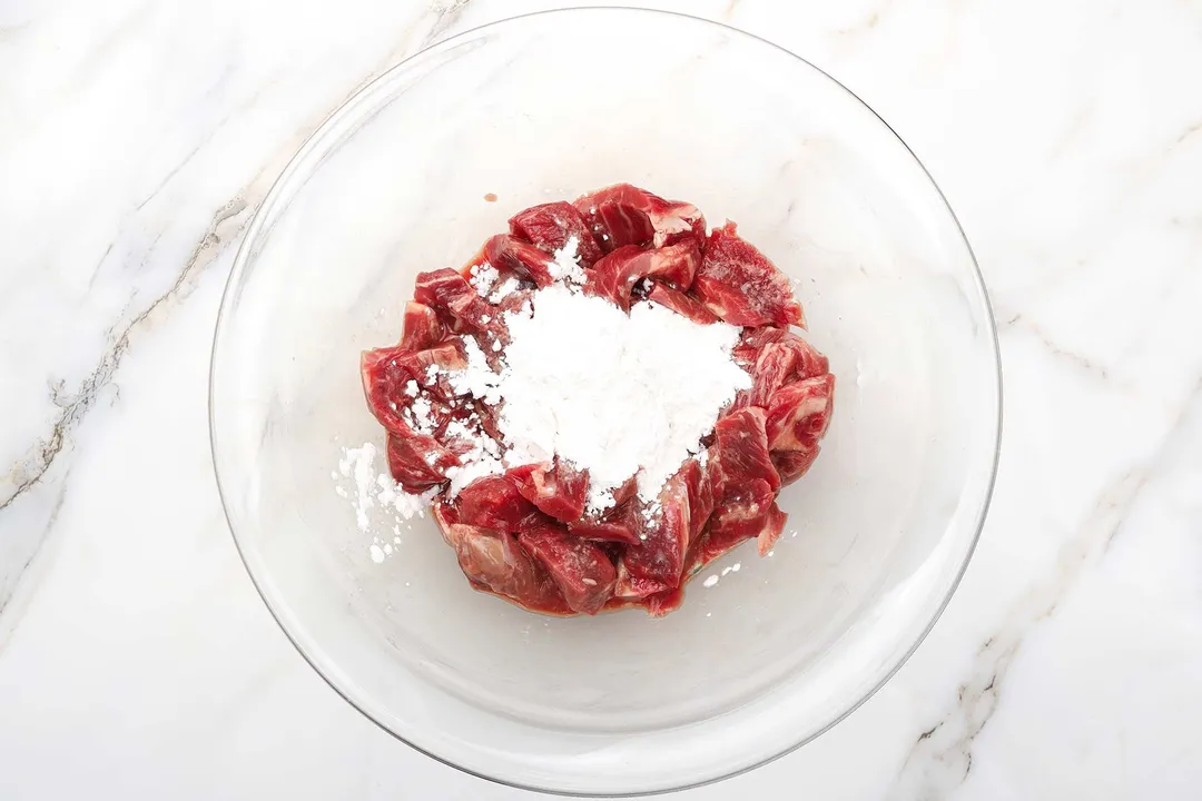 flour and sliced beef chunk in a glass bowl