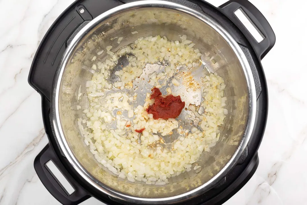 minced onion and minced garlic and tomato paste cooking in an instant pot