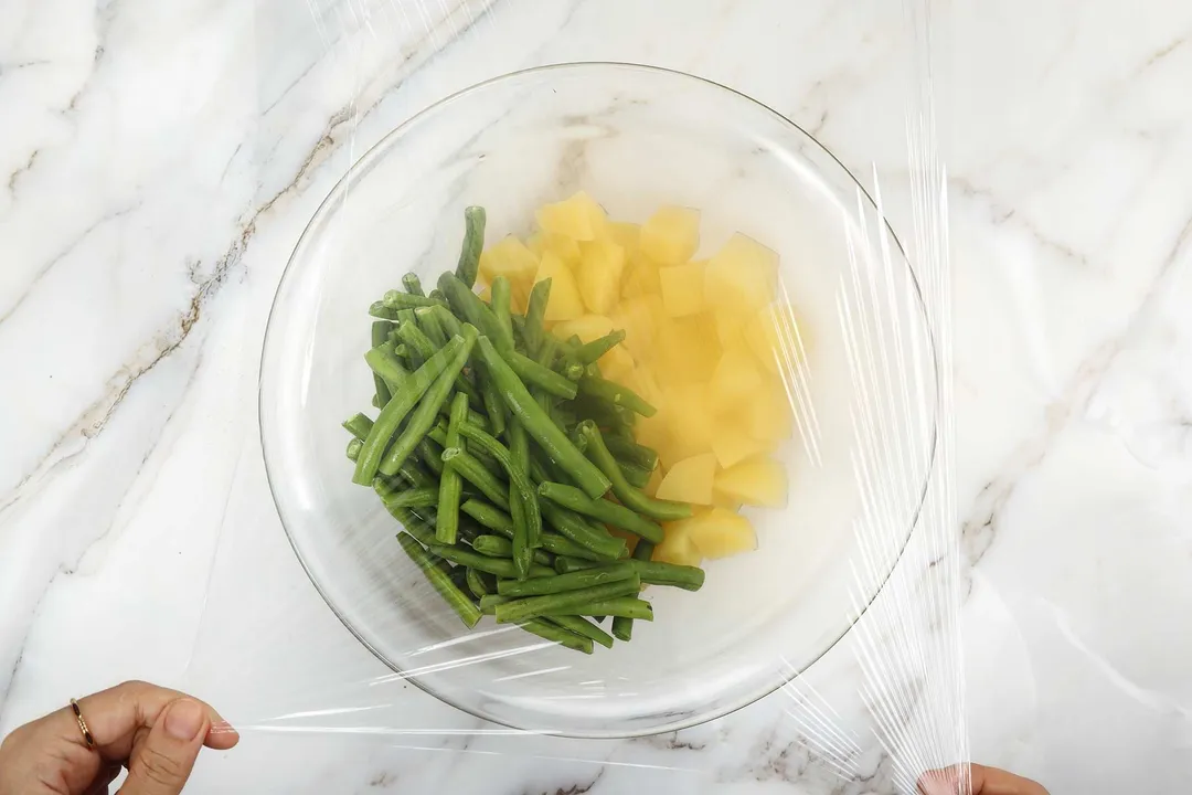 a glass bowl of potatoes cubed and green beans