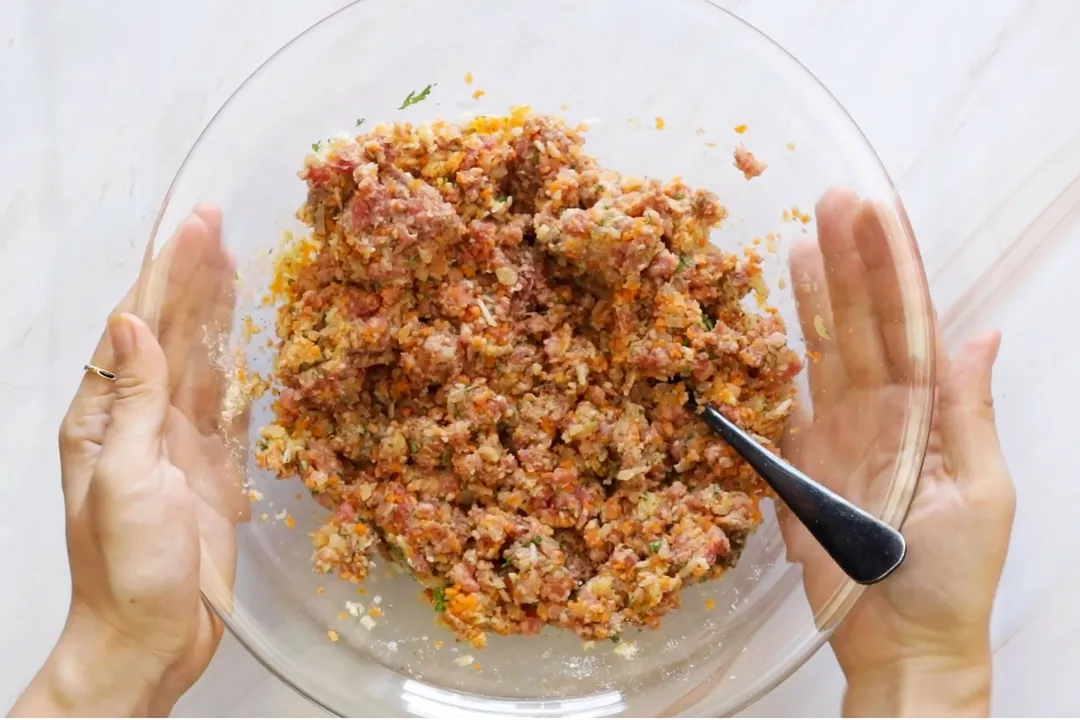 two hand holding a glass bowl of mixed ground beef with spicy