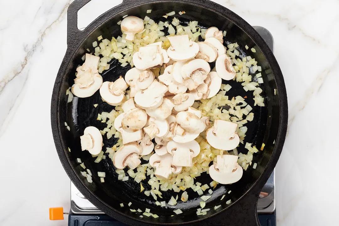 mushroom and chopped onion cooking on a cast iron skillet