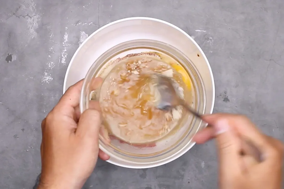 a hand holding a glass bowl, another hand holding a spoon whisking sauce