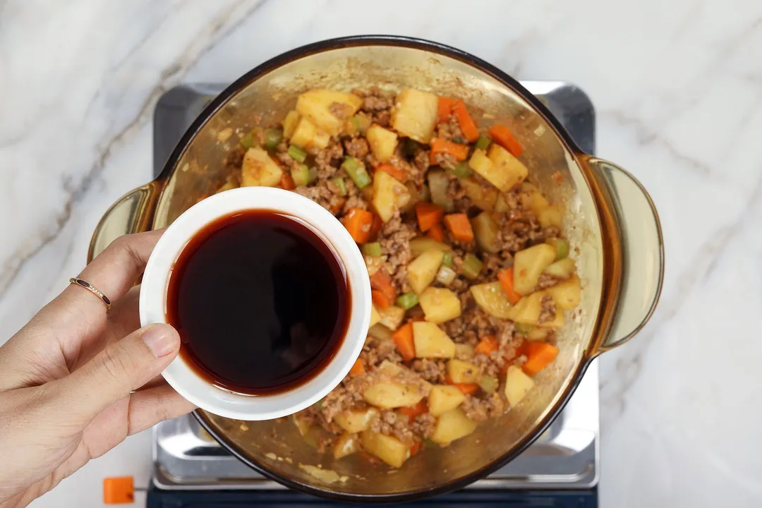 hand hold a small bowl of red wine on top of a pot of ground beef and vegetable