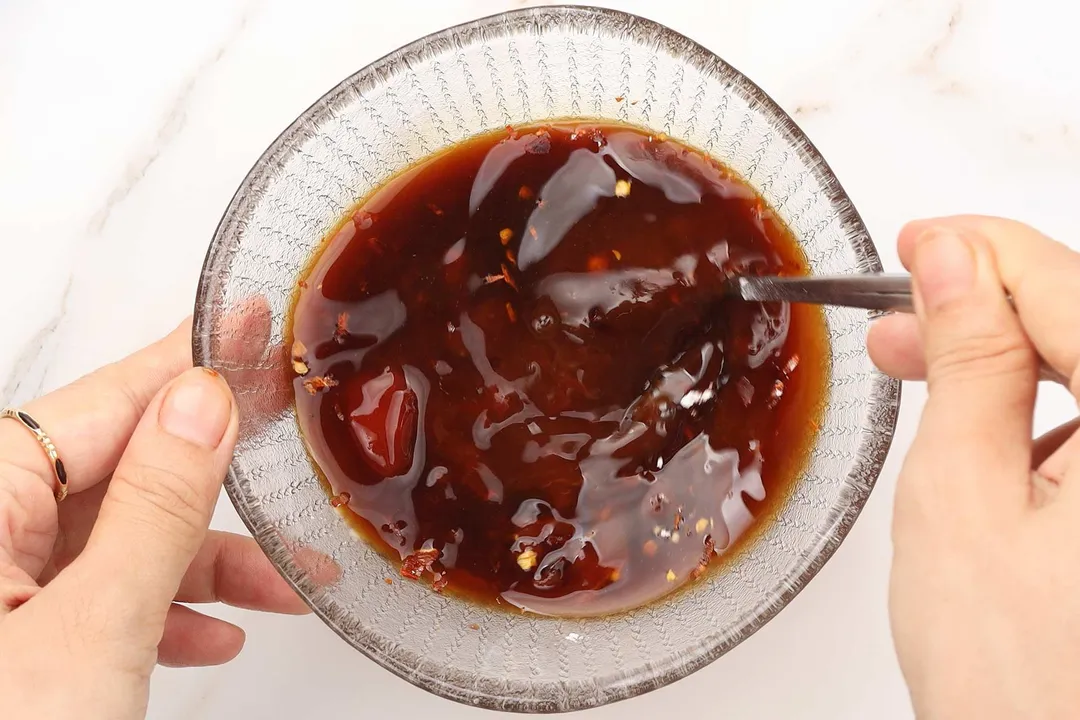 hand holding a spoon to whisk sauce