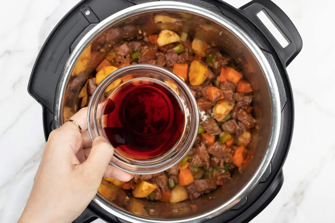 hand holding a glass bowl on top of an instant pot of beef chunk cubed, carrot and potato diced