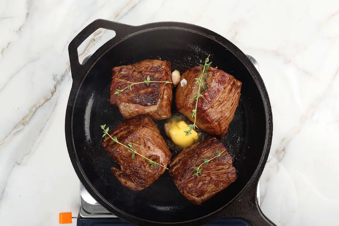 cooked beef tenderloin with butter, thyme and garlic in a cast iron skillet